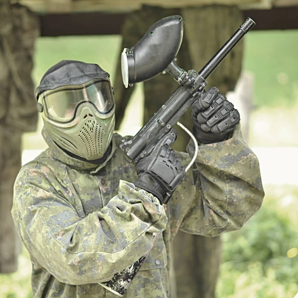 Joueur de paintball en tenue camouflage et masque, marqueur à la main, prêt pour l'action. Taches de peinture sur l'uniforme.