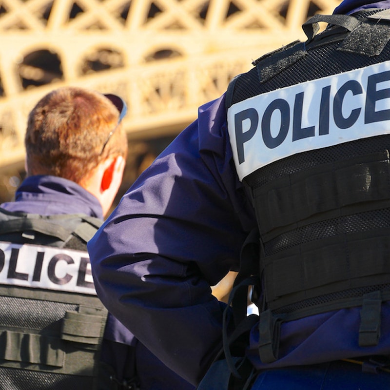 Deux policiers français avec gilets 'POLICE' sur le dos, assurant la sécurité près de la Tour Eiffel à Paris.