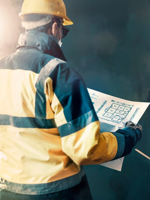 Travailleur en construction avec casque et lunettes de sécurité, de dos, analysant un plan architectural.